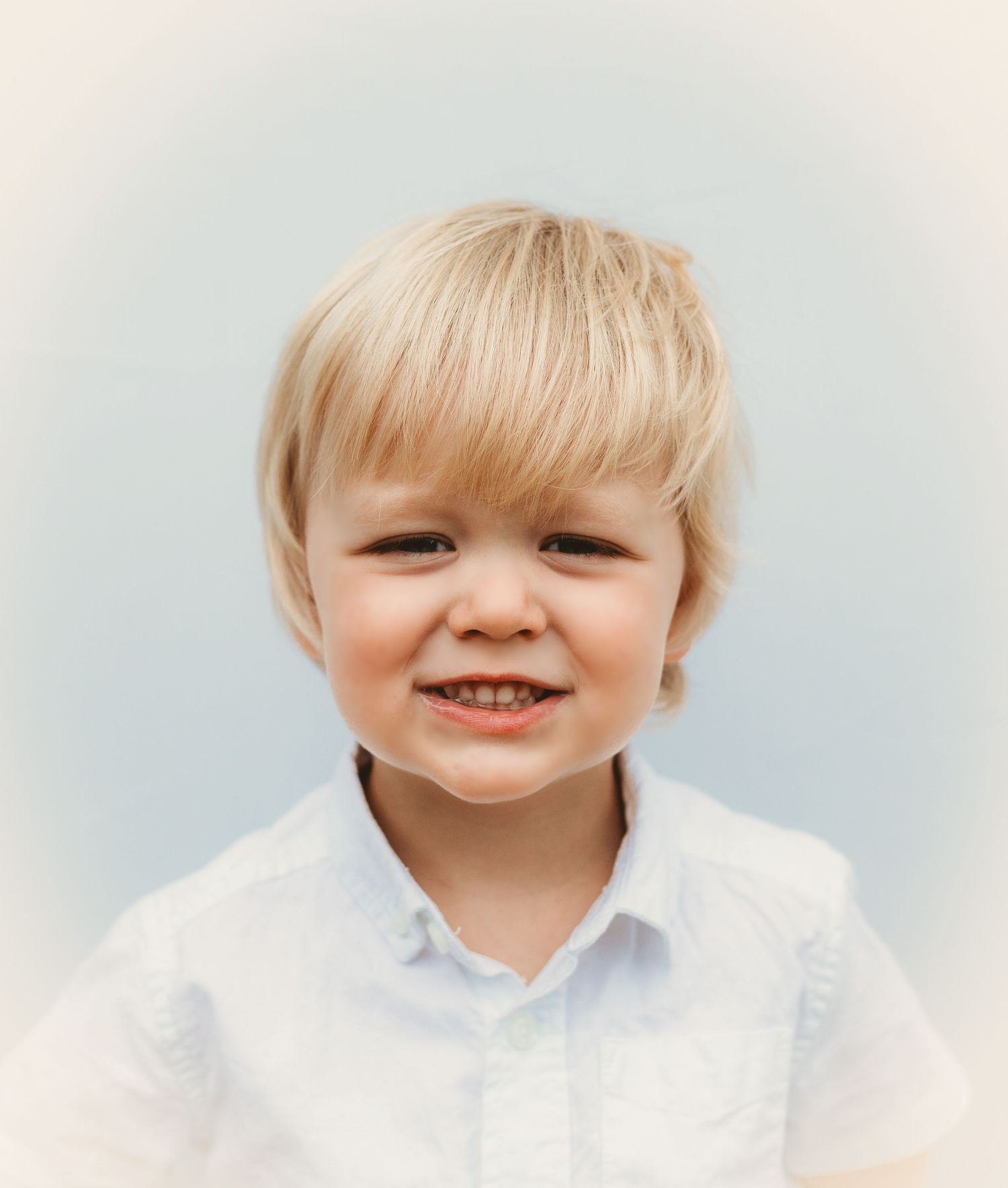 A young child with blonde hair wearing a white shirt smiles at the camera.