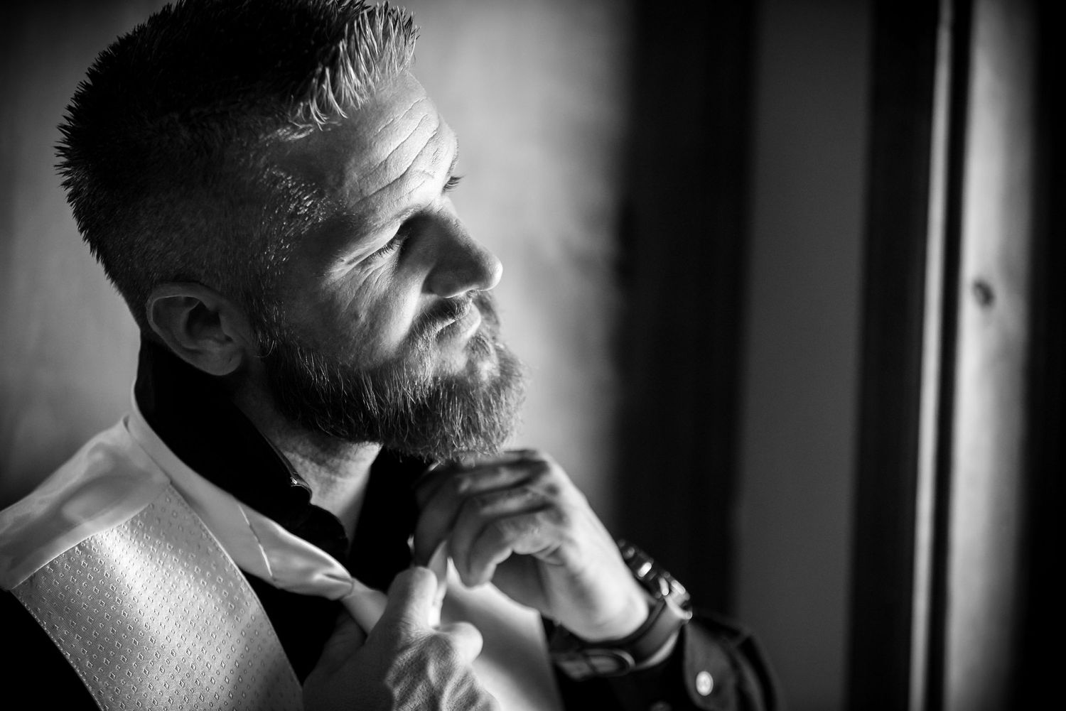 A bearded man in formal attire gazes thoughtfully into the distance in dramatic black and white lighting.