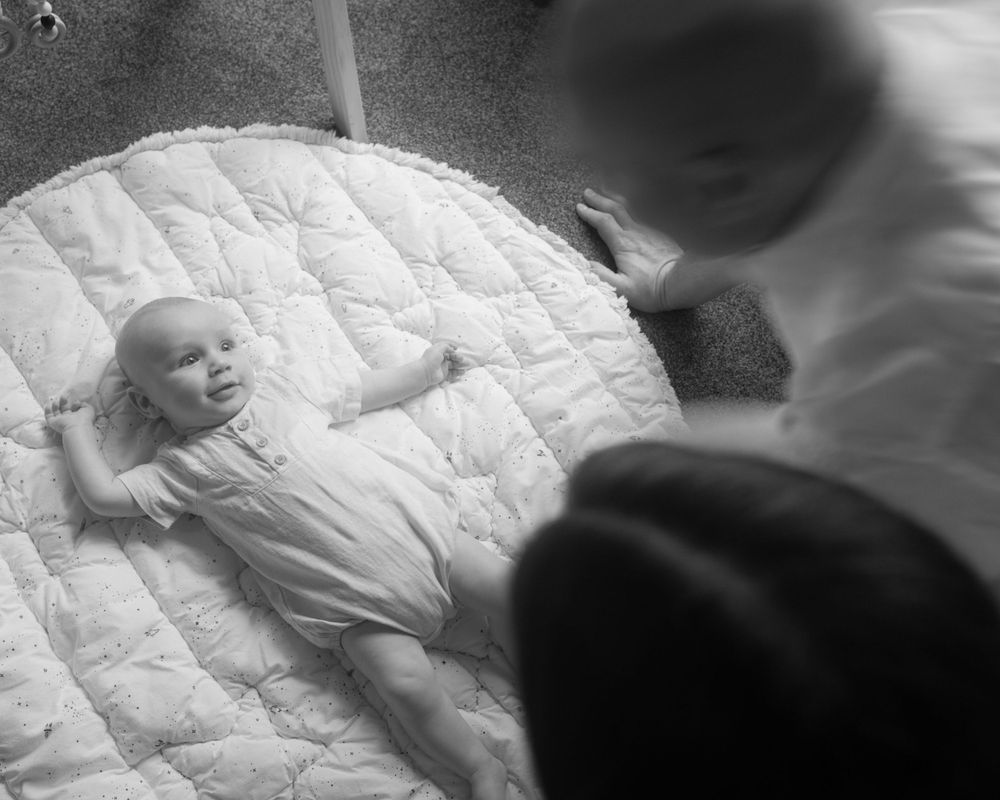 Black and white image of baby lying on quilted blanket.