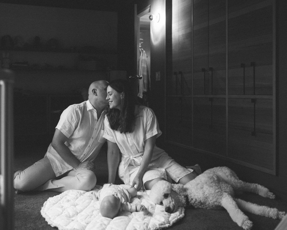 Black and white family portrait with baby and dog resting on quilted blanket.