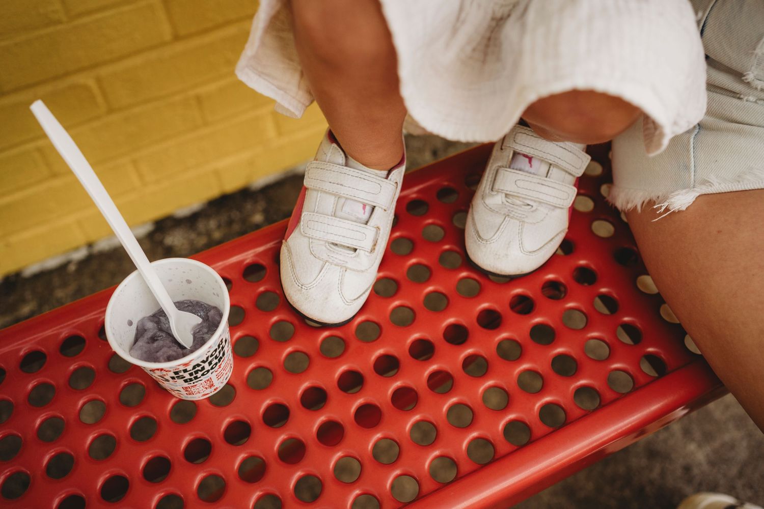 White sneakers and drink cup visible on red perforated bench surface.