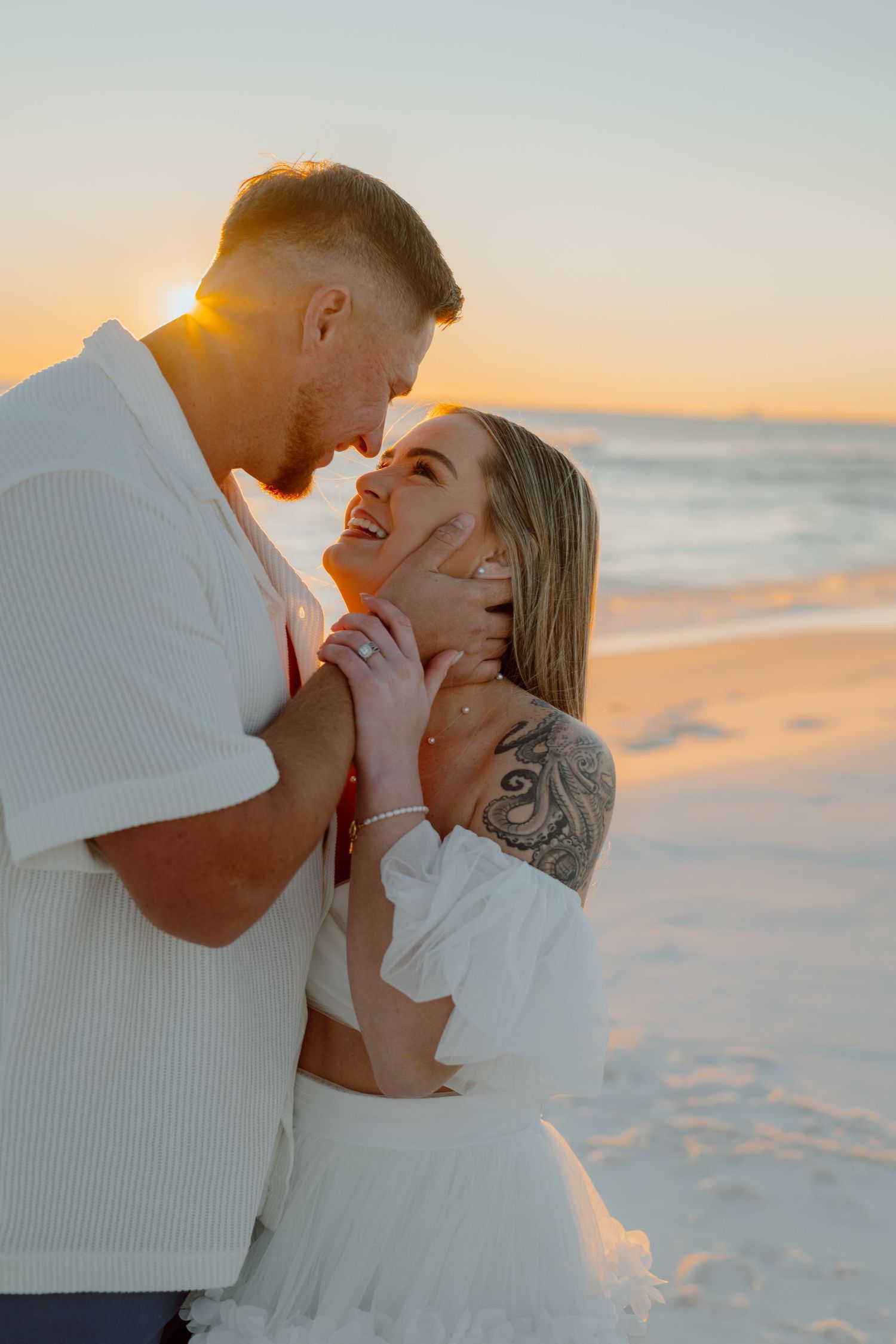 A couple embraces on a beach at sunset, sharing a romantic moment with golden light illuminating their joyful expressions.