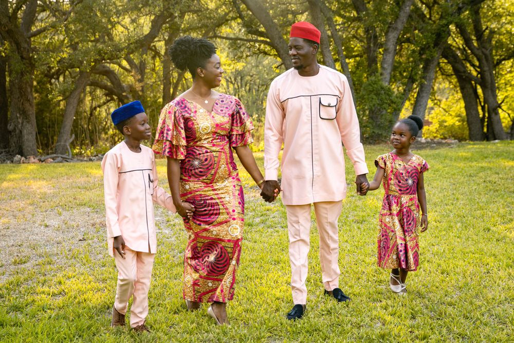 Family walking together in park wearing coordinated pink and patterned traditional attire.
