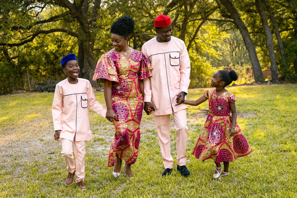 Happy family strolling through park in matching pink and patterned African-inspired outfits.