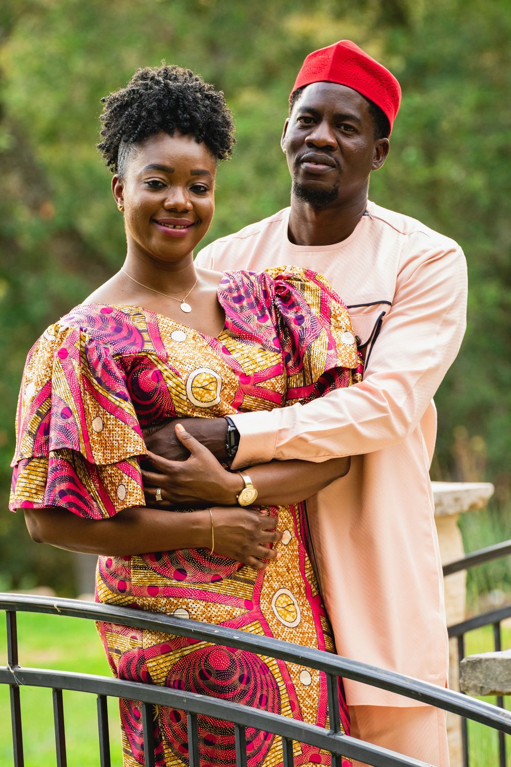 Couple embracing on bridge wearing coordinated African print clothing and pink tones.