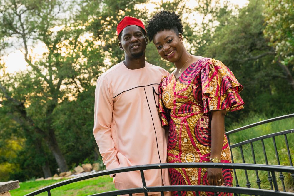 Couple posing on bridge wearing coordinated pink and patterned traditional outfits.