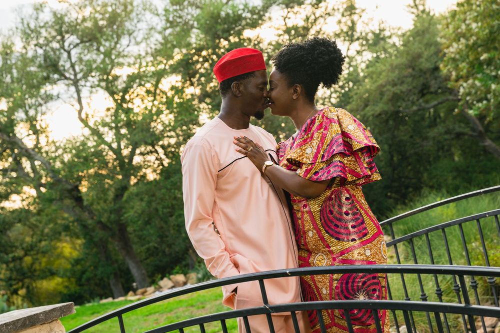 A romantic couple in traditional African attire share a tender moment on a bridge at sunset.