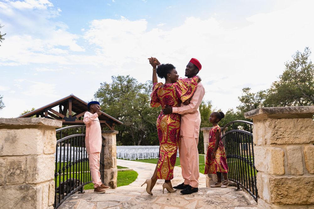 A couple in pink and red traditional dress dance together by an ornate stone gate.