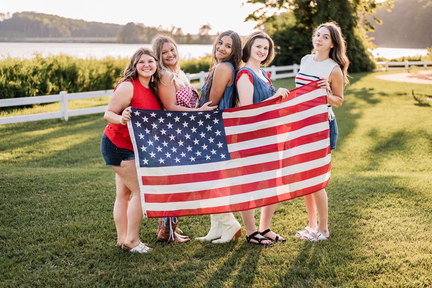 Group of people holding American flag in sunny grassy field during golden hour.