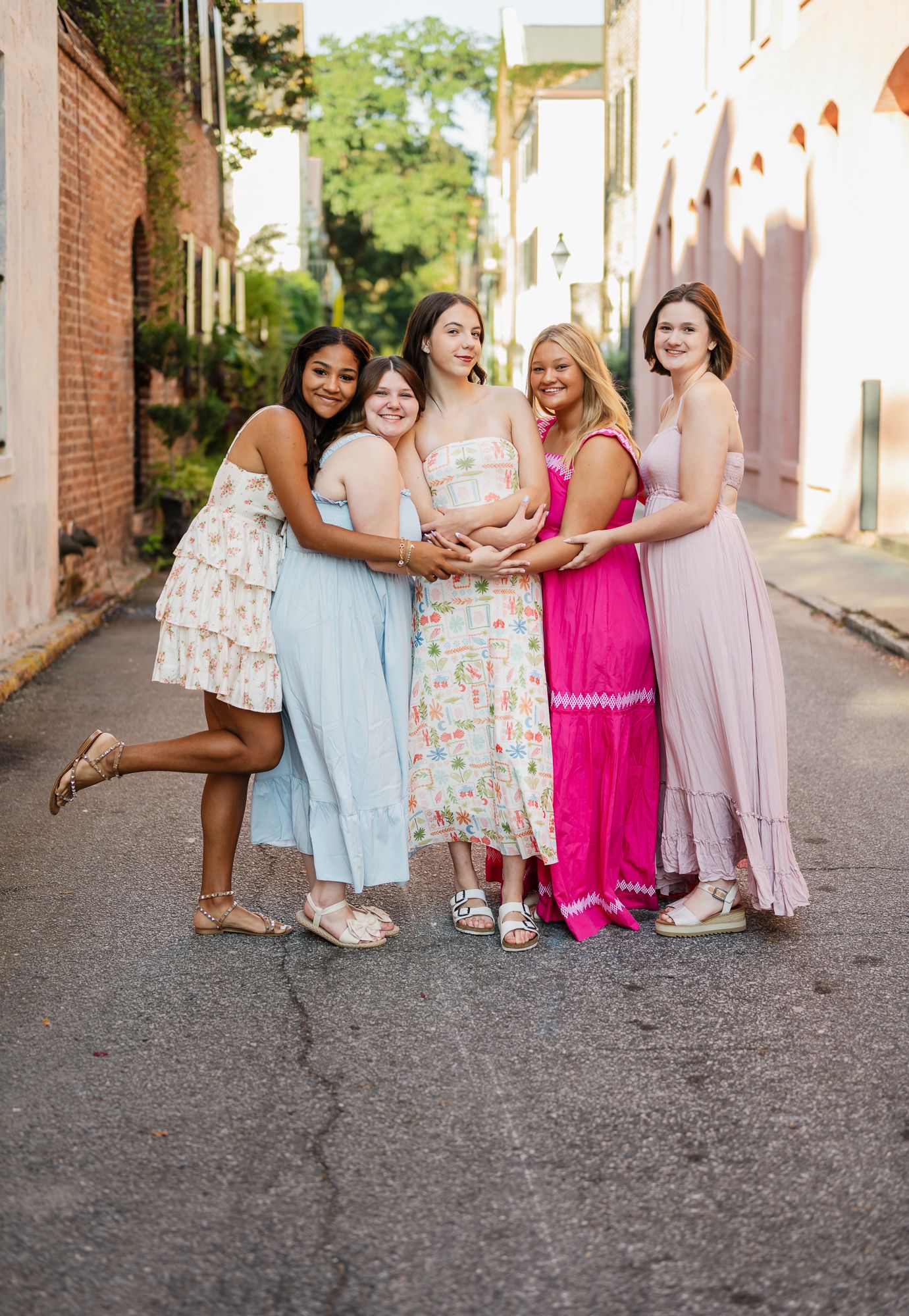A group in colorful dresses poses together on a charming cobblestone street during a photo session.