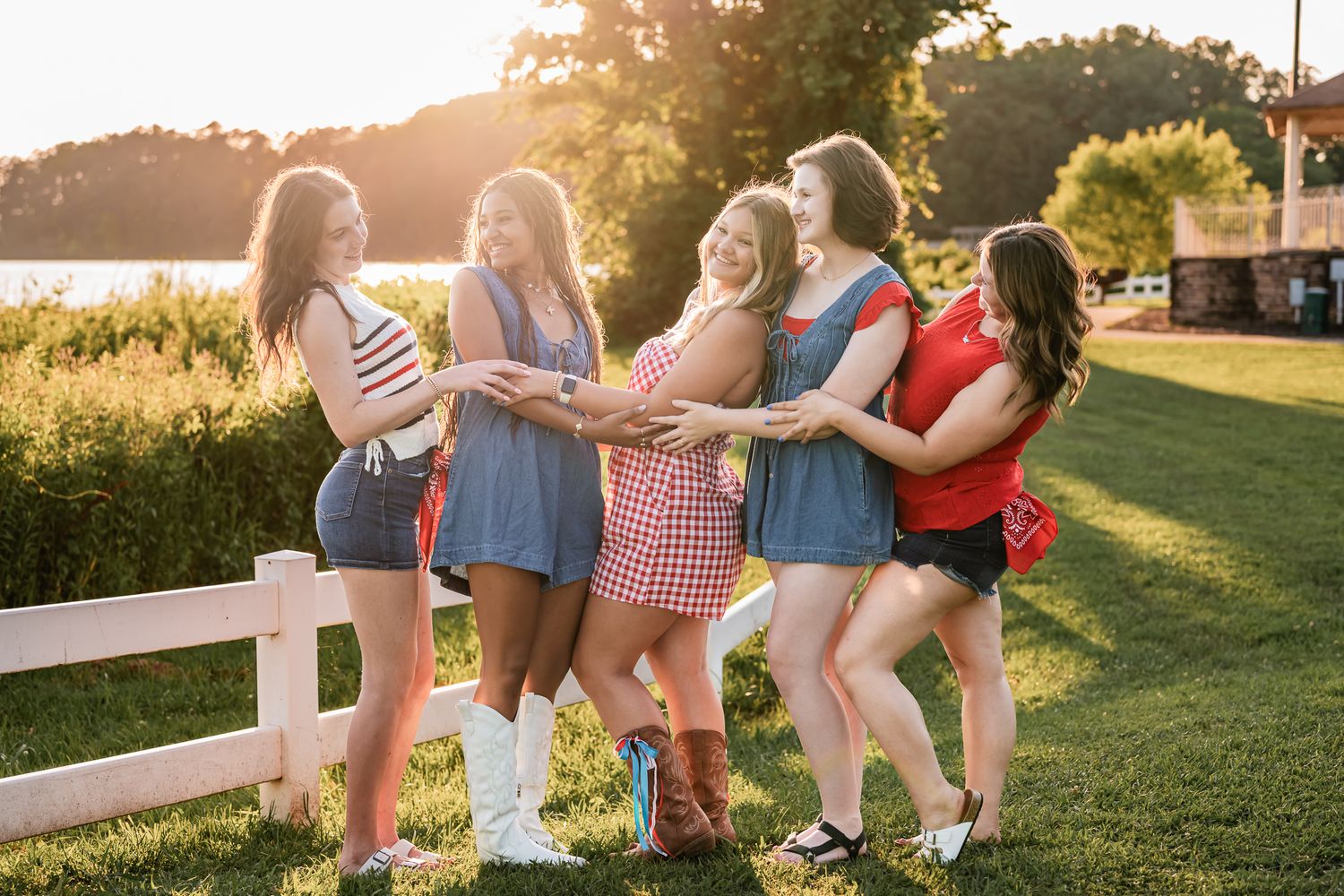 A group of people in casual summer outfits walking together on a grassy path during golden hour sunset.