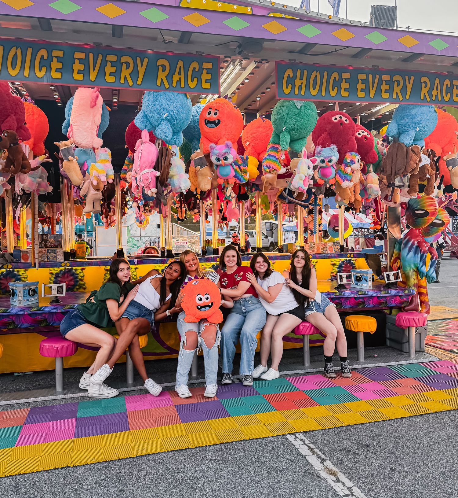 Colorful carnival game booth with stuffed animal prizes and rainbow decorations at a fairground.