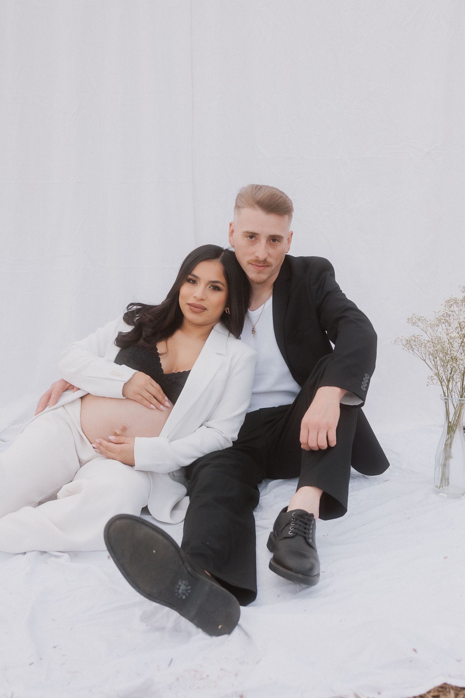 Modern maternity photo with couple in contrasting outfits on white backdrop.