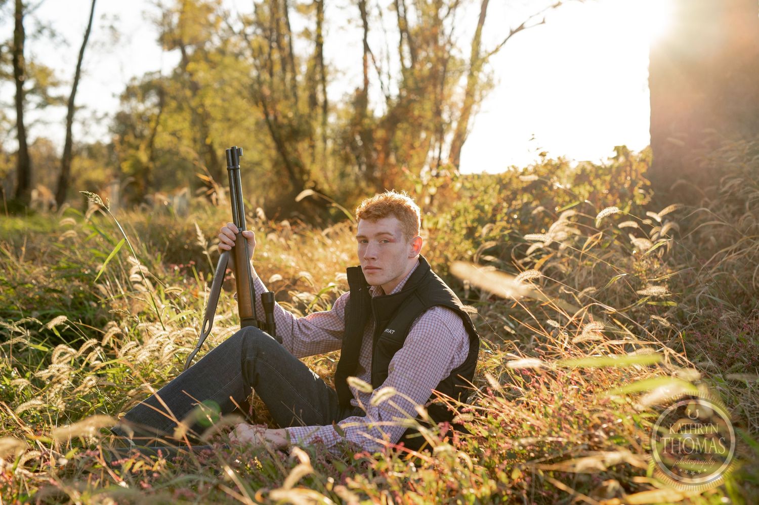 Person sitting with hunting rifle in sunlit autumn field.