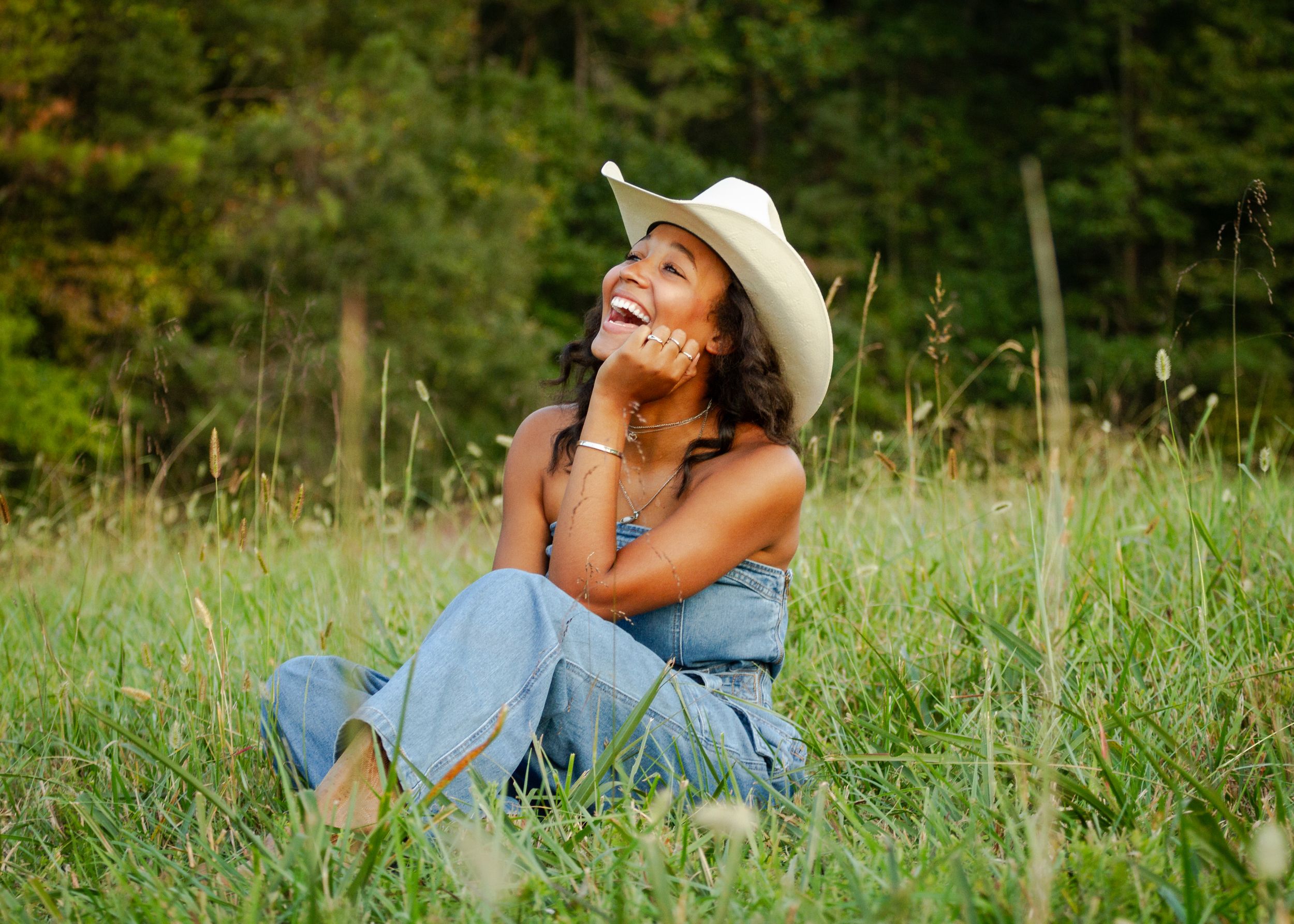 Girl in cowboy hat sitting in a green grassy field