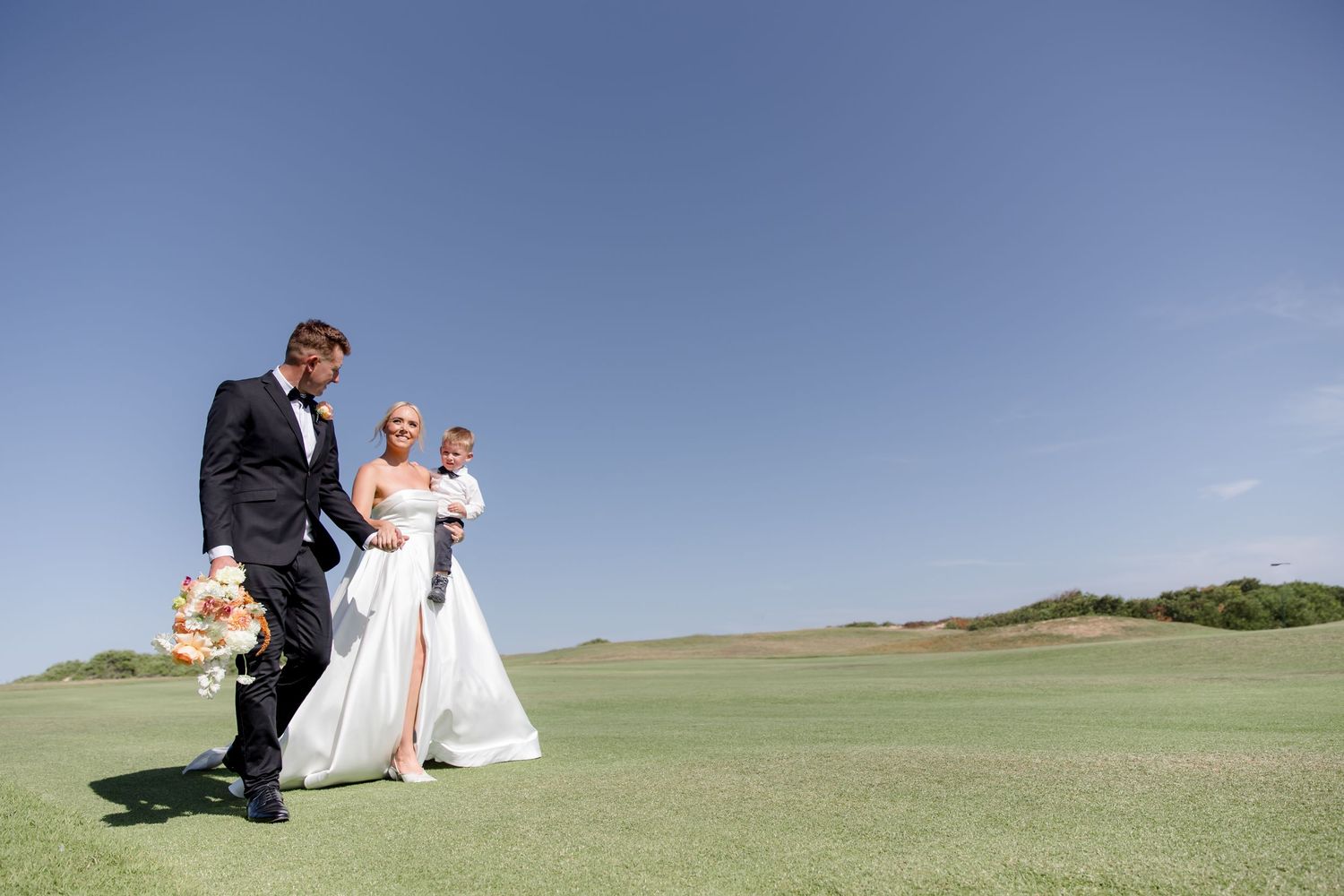 A wollongong golf club wedding captured on a sunny and warm day, the bride and groom is walking with their son across the green