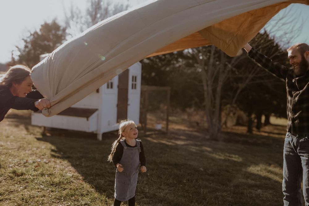 A white sheet billows in the sunlight as people play underneath it.