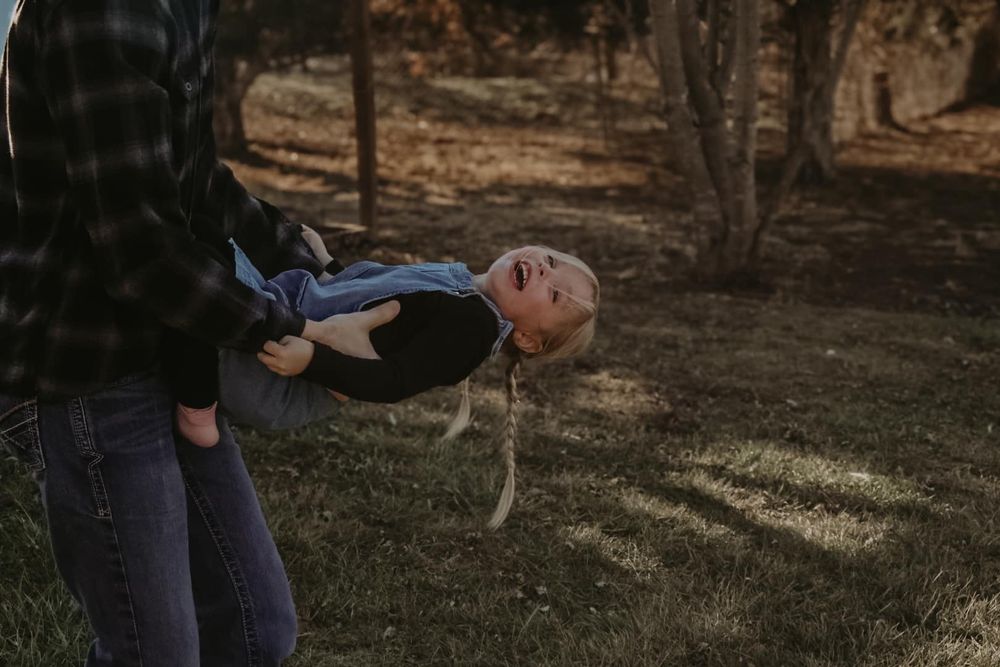 A playful moment captured as someone is held horizontally in dappled sunlight.