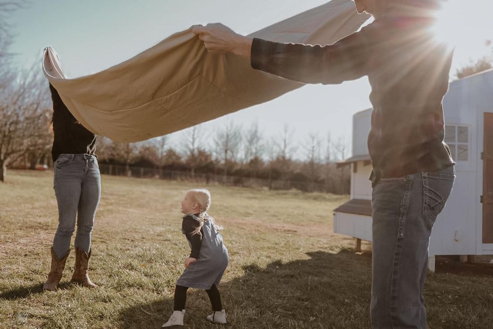 A child ducks under a tan sheet held up in the golden afternoon sunlight.