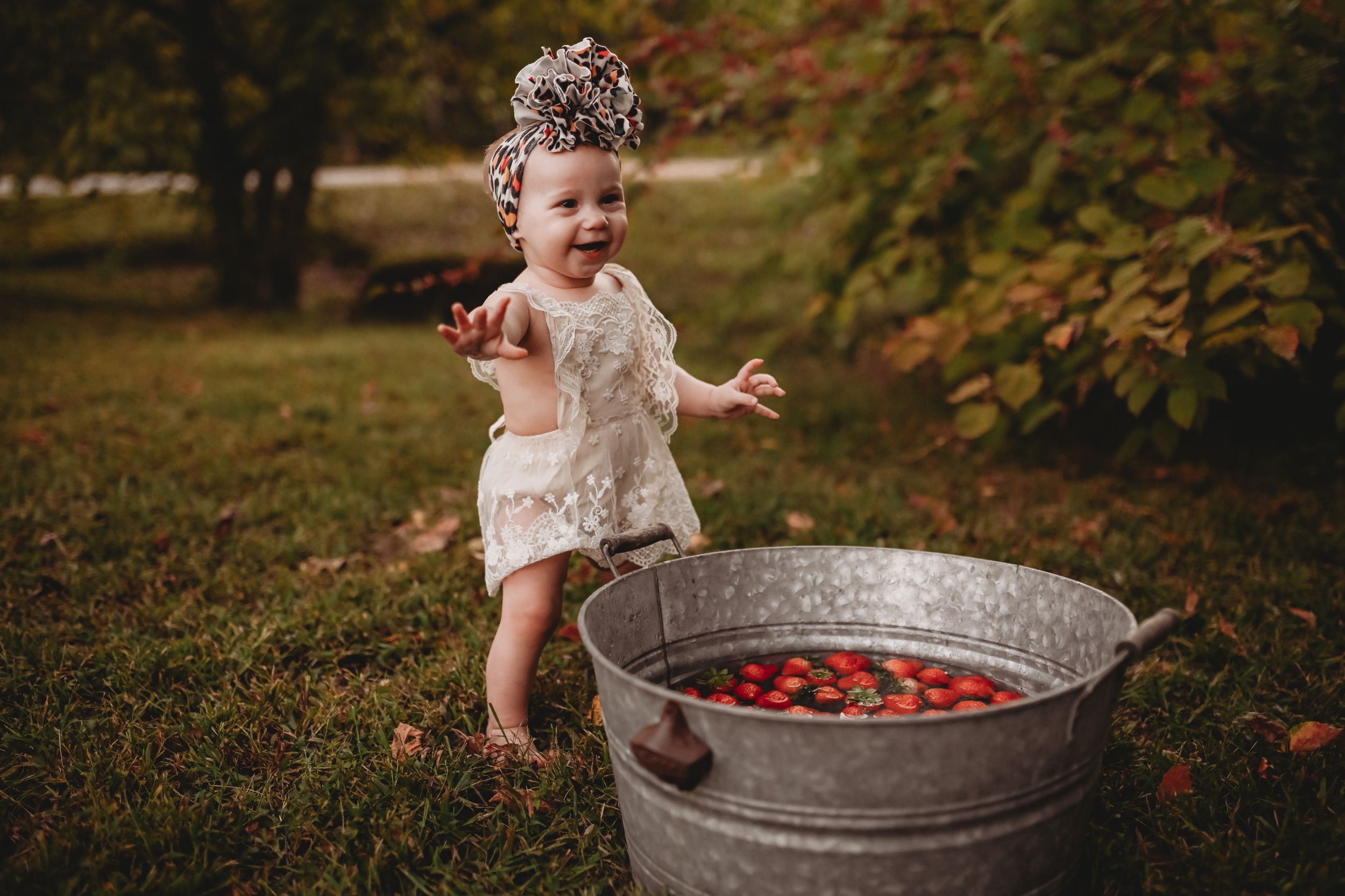A toddler plays in a metal tub filled with red apples during an autumn outdoor photoshoot.
