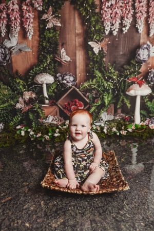 Baby on sparkly blanket with whimsical woodland backdrop featuring mushrooms and greenery.