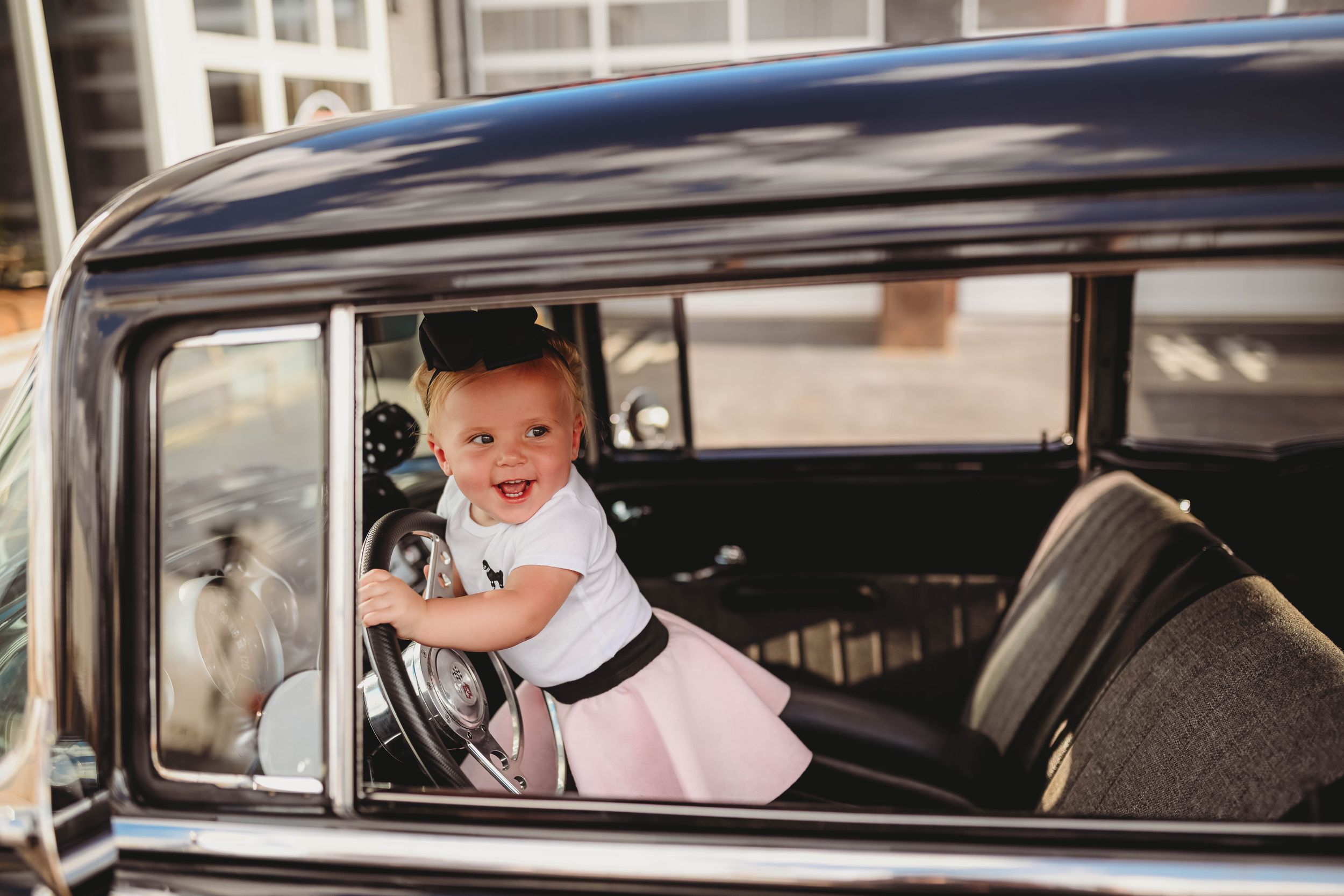 Baby looking through window of vintage black car.