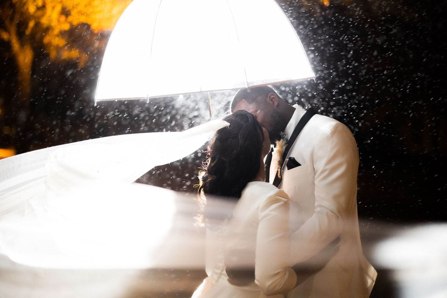Silhouetted couple embraces under dramatic backlighting at a wedding celebration.