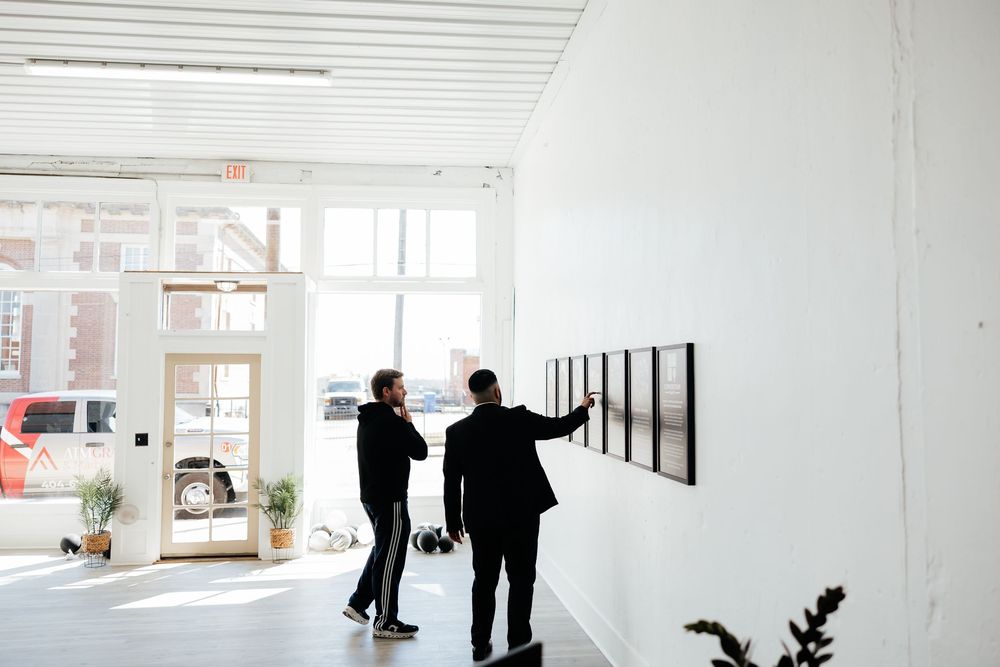 Two people walk through a modern white gallery space with artwork displayed on the walls.