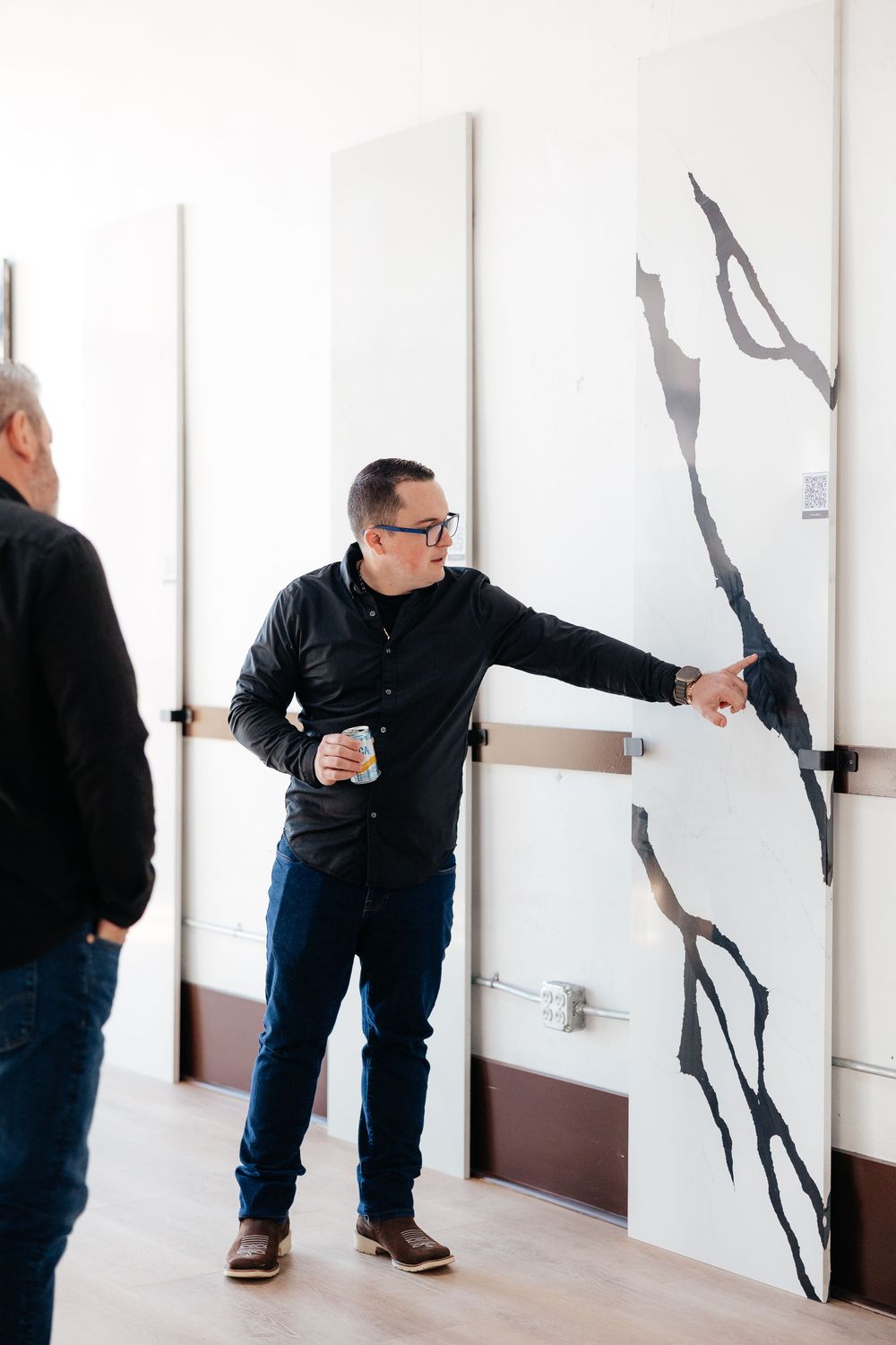 A person in black clothing and jeans examines a wall display showing dark branch-like patterns.
