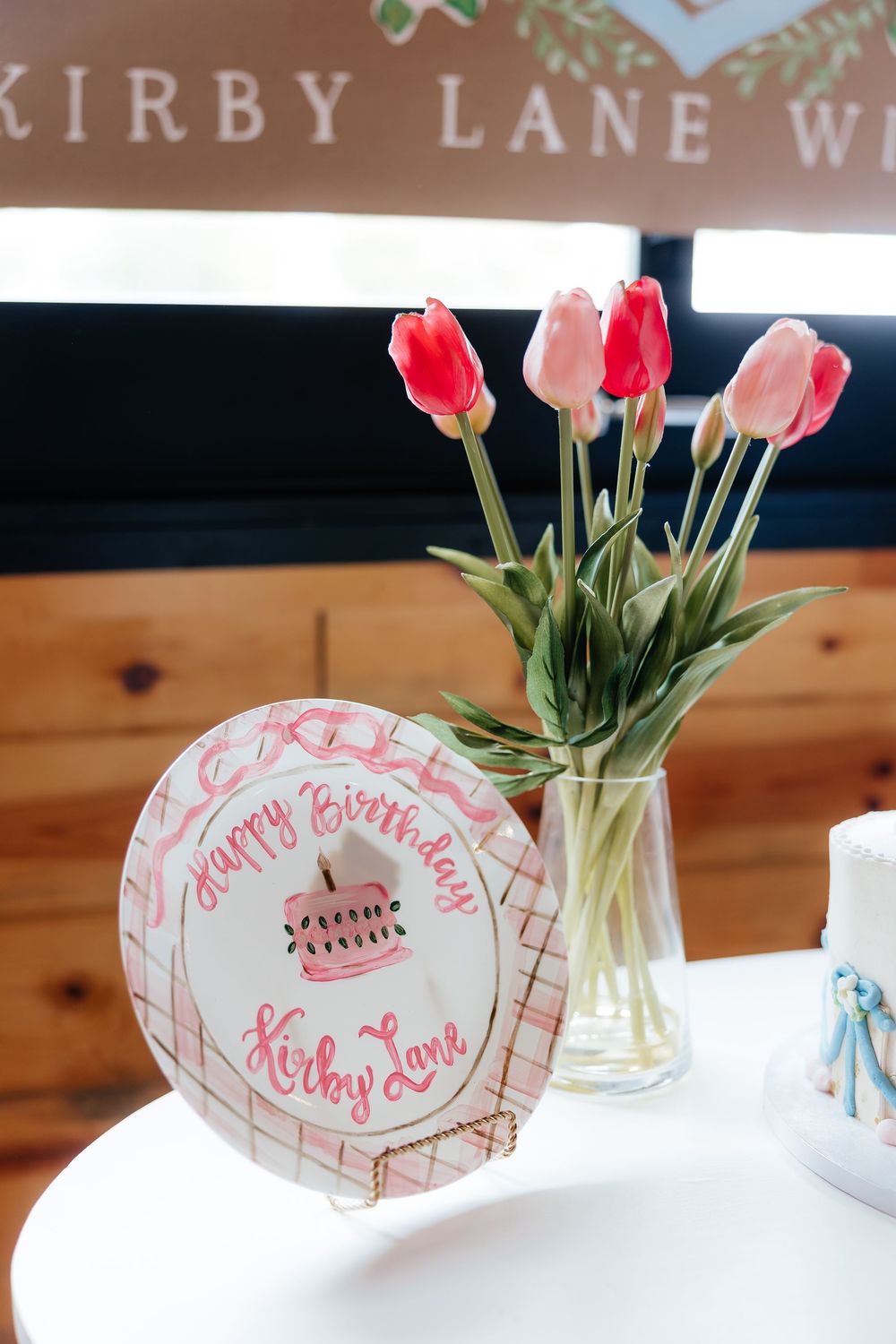 Happy Birthday Kirby Lane plate with pink tulips in a glass vase on a white table at a birthday celebration.