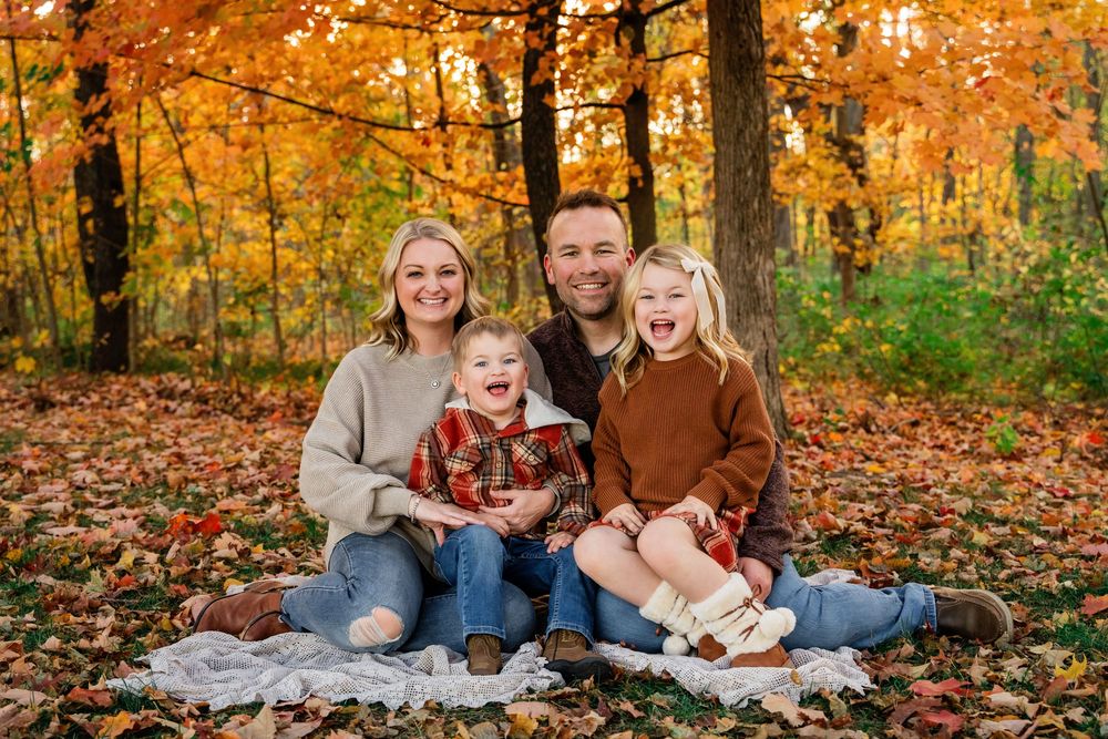 Happy family of four sitting on a blanket surrounded by colorful fall leaves in the forest.