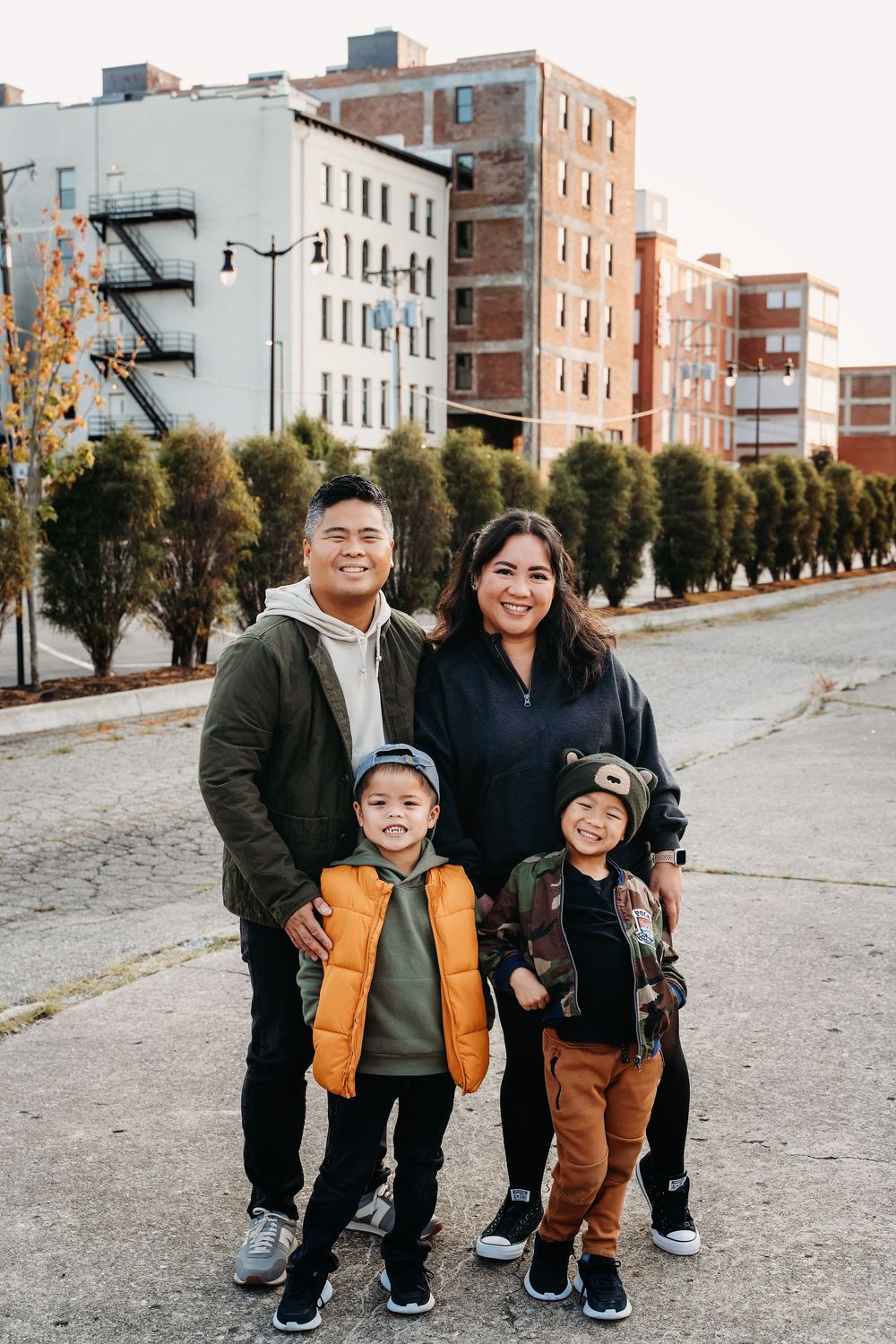Happy Family of four smiling together on urban street with city buildings in background.