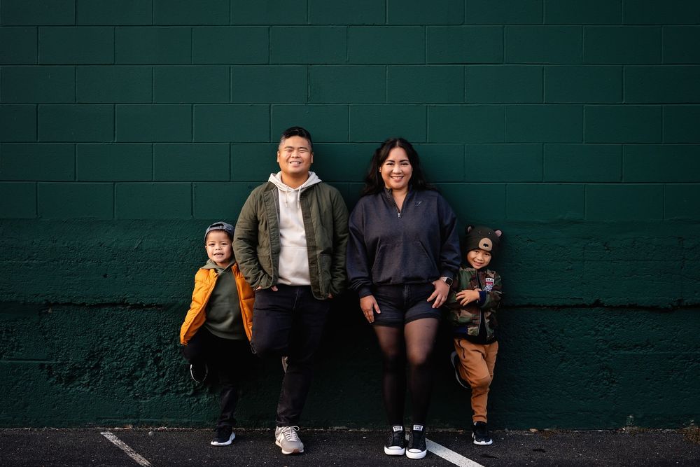 Family of four posing casually against a dark green wall outdoors.