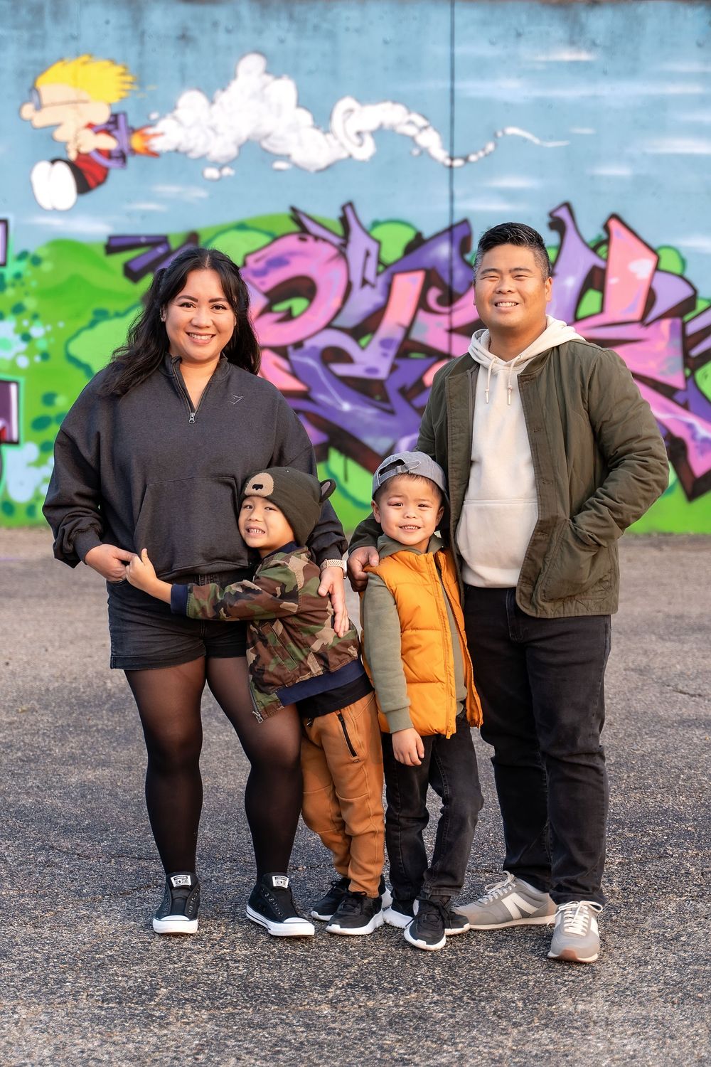 Family of four posing in front of colorful graffiti wall outdoors.
