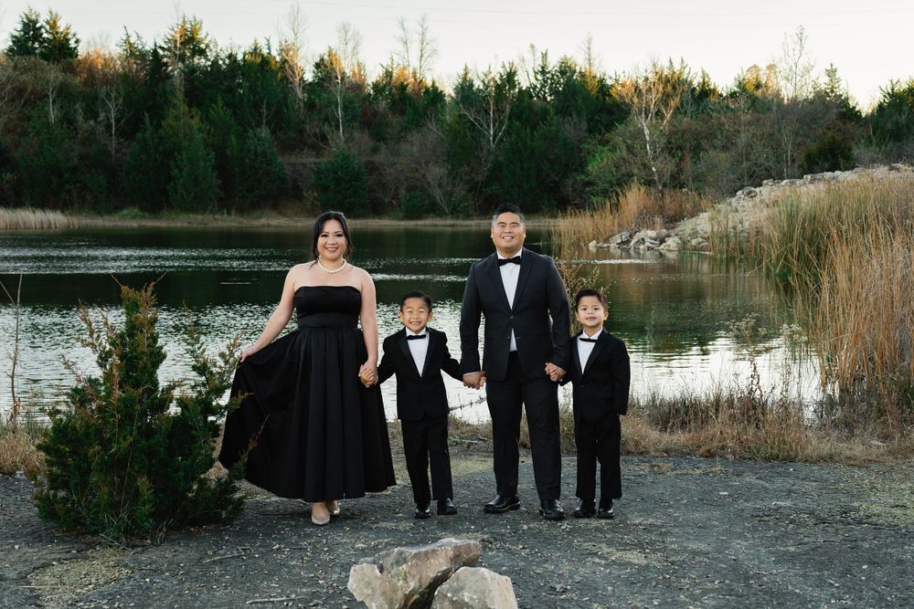 Family of four in elegant black formal wear posing by a serene lake surrounded by autumn trees.