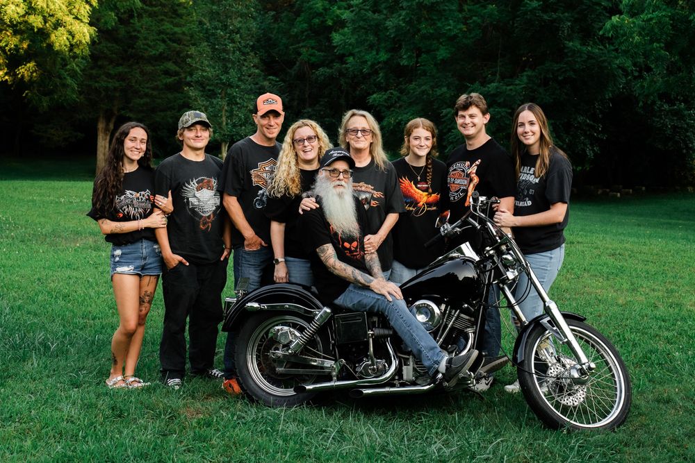 Large family group in matching Harley-Davidson shirts posing outdoors with a classic motorcycle.
