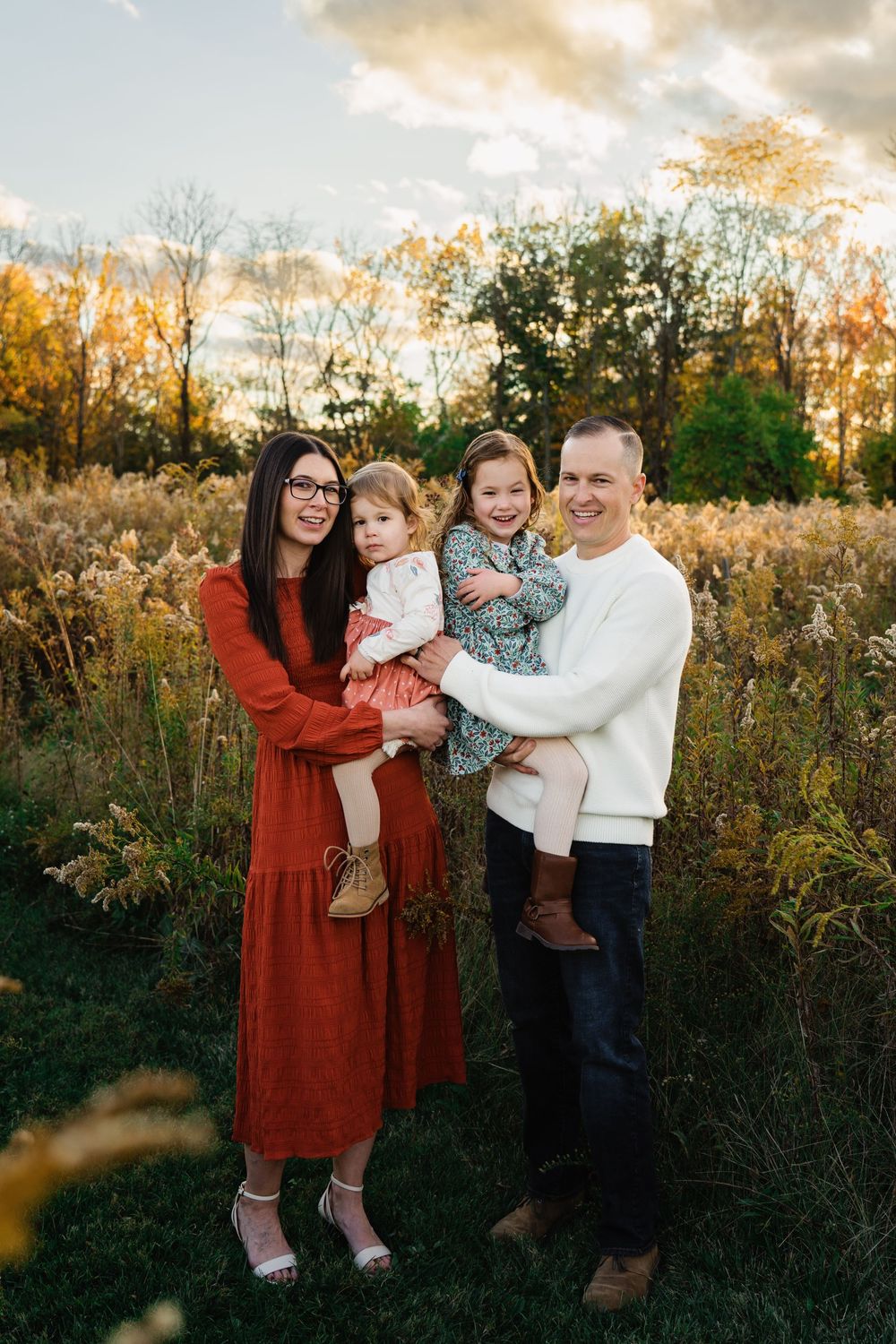 Happy family of four standing in a golden field at sunset during autumn family portraits.