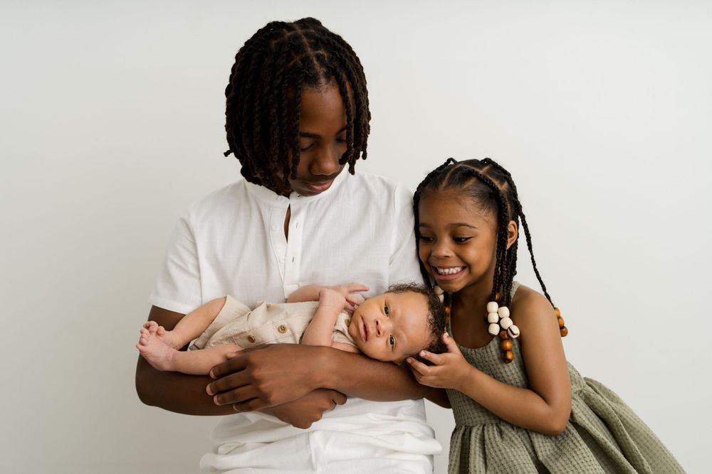 Teenage boy and young girl lovingly holding a sleeping newborn baby in a white studio portrait.