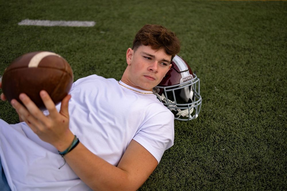 A football player in white uniform throws a ball during practice on a grass field.