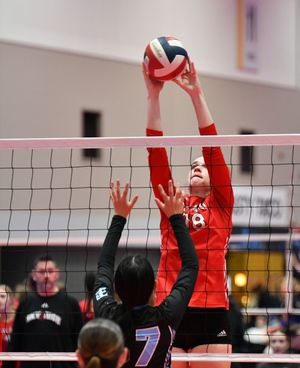 Volleyball player in red uniform reaches up to block at the net during competitive indoor match.