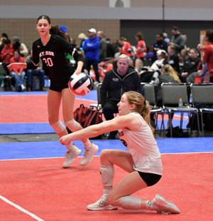 Indoor volleyball player in white jersey performs defensive dive on red court during competitive match.