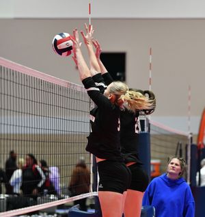 Indoor volleyball player jumps to block the ball at the net during competitive match.