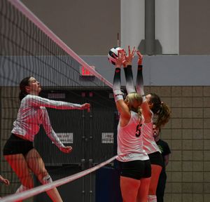 Women's volleyball players competing at the net with one attempting a spike and others defending the play.