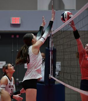 Volleyball players at the net jump up to block and spike during an intense indoor match.