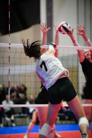 Players executing an impressive defensive volleyball block at the net during an intense indoor volleyball match.