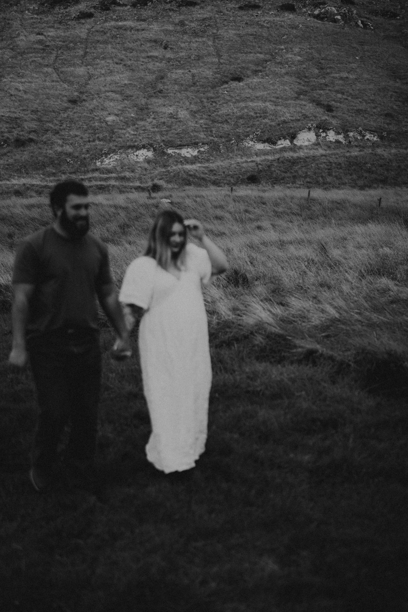 A couple holding hands in a grassy field photographed in moody black and white.