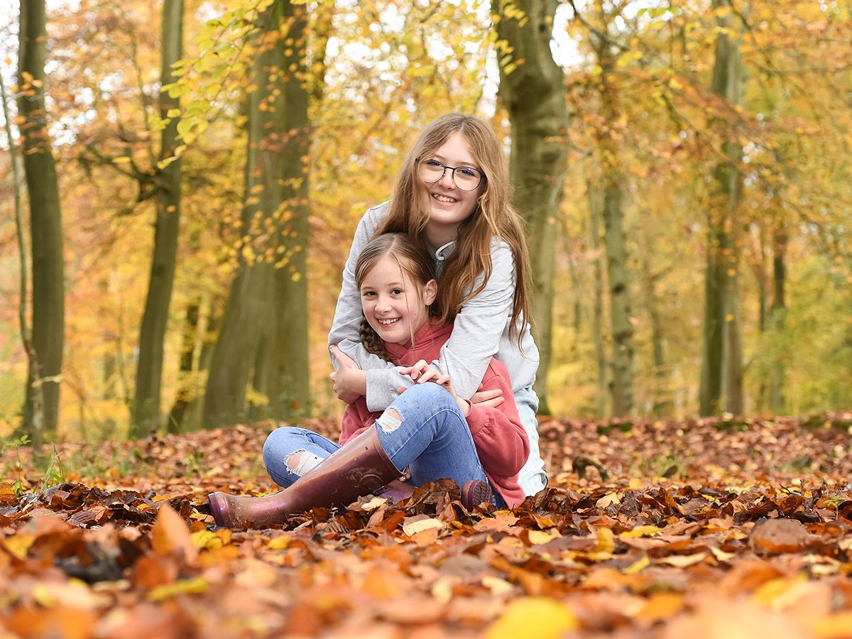 Two girls on the forest floor in autumn, enjoying nature in Bradenham Woods, captured by Family Photographer Abigail's Studio.