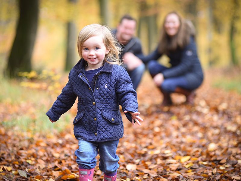 A young girl in a blue jacket and pink boots walks through colourful autumn leaves, Bradenham Woods captured by Abigail's Studio.