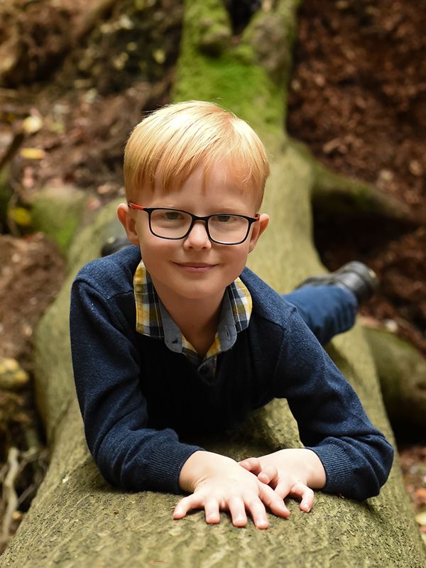 A young boy with glasses sits on a log in Bradenham Woods captured by Abigail's Studio Family Photographer.