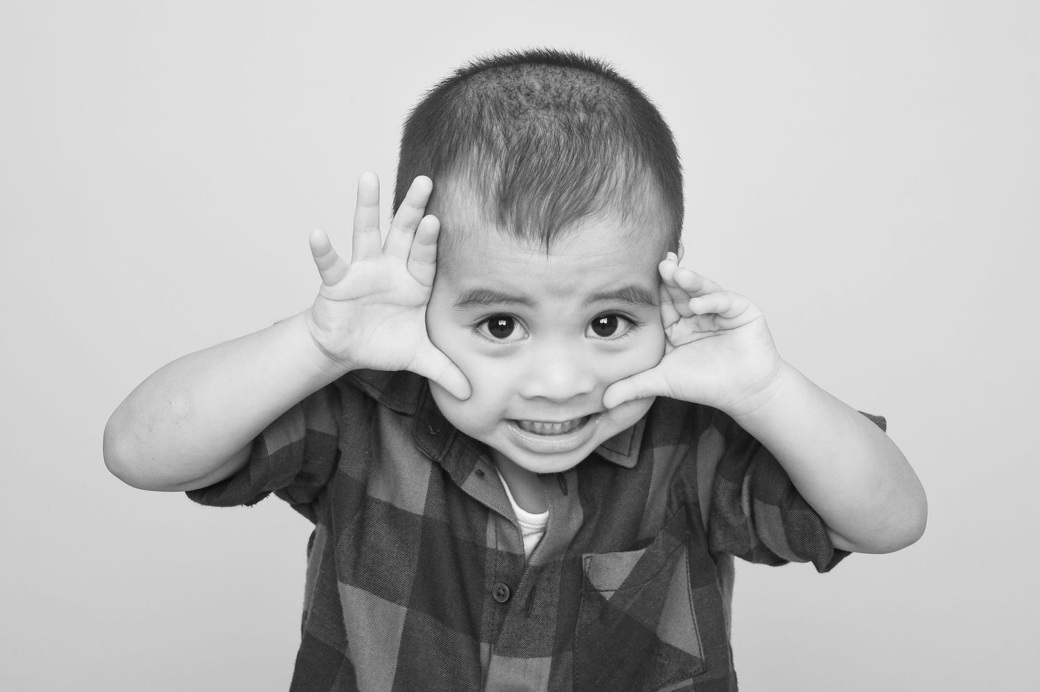 A young boy creatively uses his hands to make a face, as captured by Abigail's Studio Family Photographer in High Wycombe.